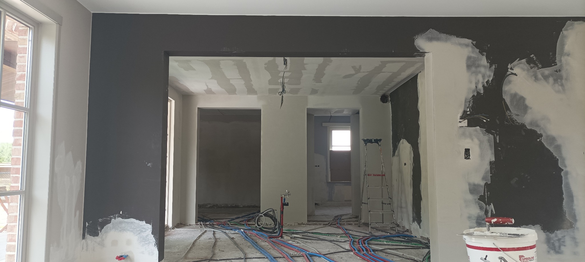 Wnętrze w trakcie remontu: szpachlowane ściany, widoczne instalacje, drabina. Ściany częściowo pomalowane na ciemny kolor, sufit przygotowany do malowania.