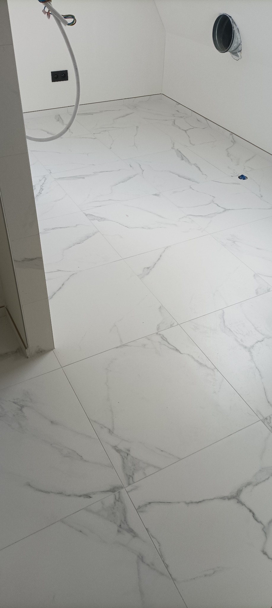 Białe, marmurowe płytki podłogowe w jasnym pomieszczeniu z widoczną instalacją wentylacyjną i elektryczną. Minimalistyczny design, świeżo położona podłoga.