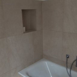 Dariusz Leśniewski L-DAR-BUD - Beżowa łazienka po remoncie: wanna, płytki i wnęka w ścianie. Minimalistyczny design, jasne wnętrze. Widok na fragment baterii wannowej.