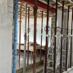 Dariusz Leśniewski L-DAR-BUD - Wnętrze w trakcie remontu: podpory stropowe, instalacja w ścianie, surowy beton. Widoczne narzędzia i drabina. Prace przygotowawcze do wykończenia.