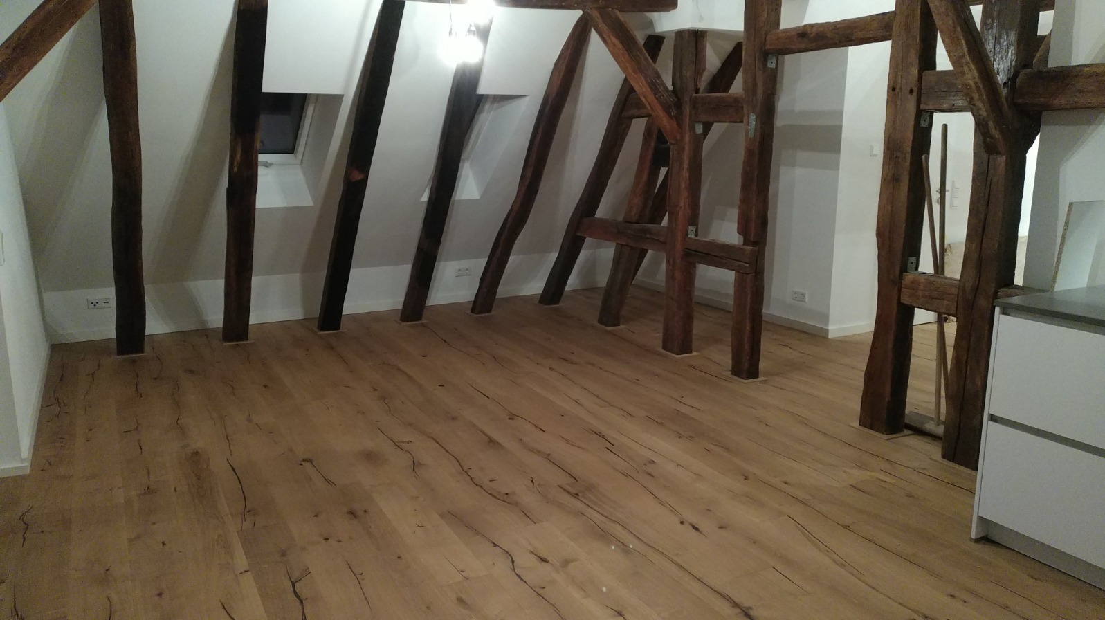 Jasna podłoga z paneli drewnopodobnych w pokoju na poddaszu z drewnianymi belkami konstrukcyjnymi. Widoczne gniazdka elektryczne przy podłodze.