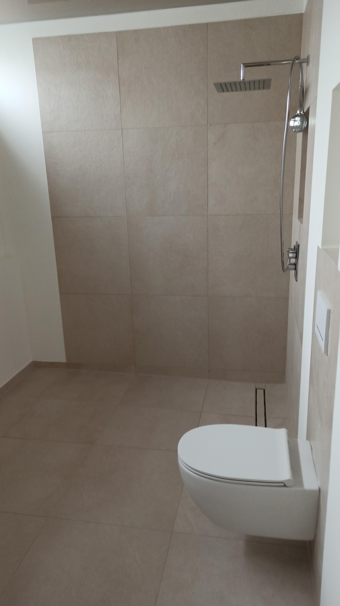 Beżowa łazienka z kabiną typu walk-in i podwieszaną toaletą. Minimalistyczny design, płytki w odcieniach beżu, nowoczesna armatura. Widoczny odpływ liniowy.