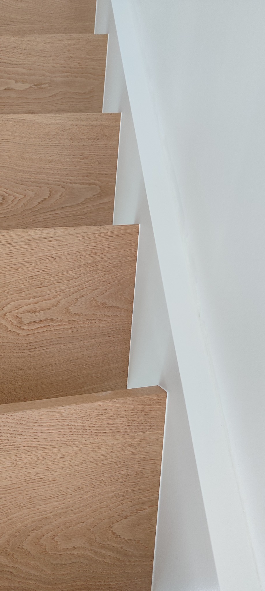 Jasne, drewniane schody z białymi podstopnicami, widziane z góry pod kątem. Minimalistyczny design, czyste linie, nowoczesne wykończenie. Detal schodów.