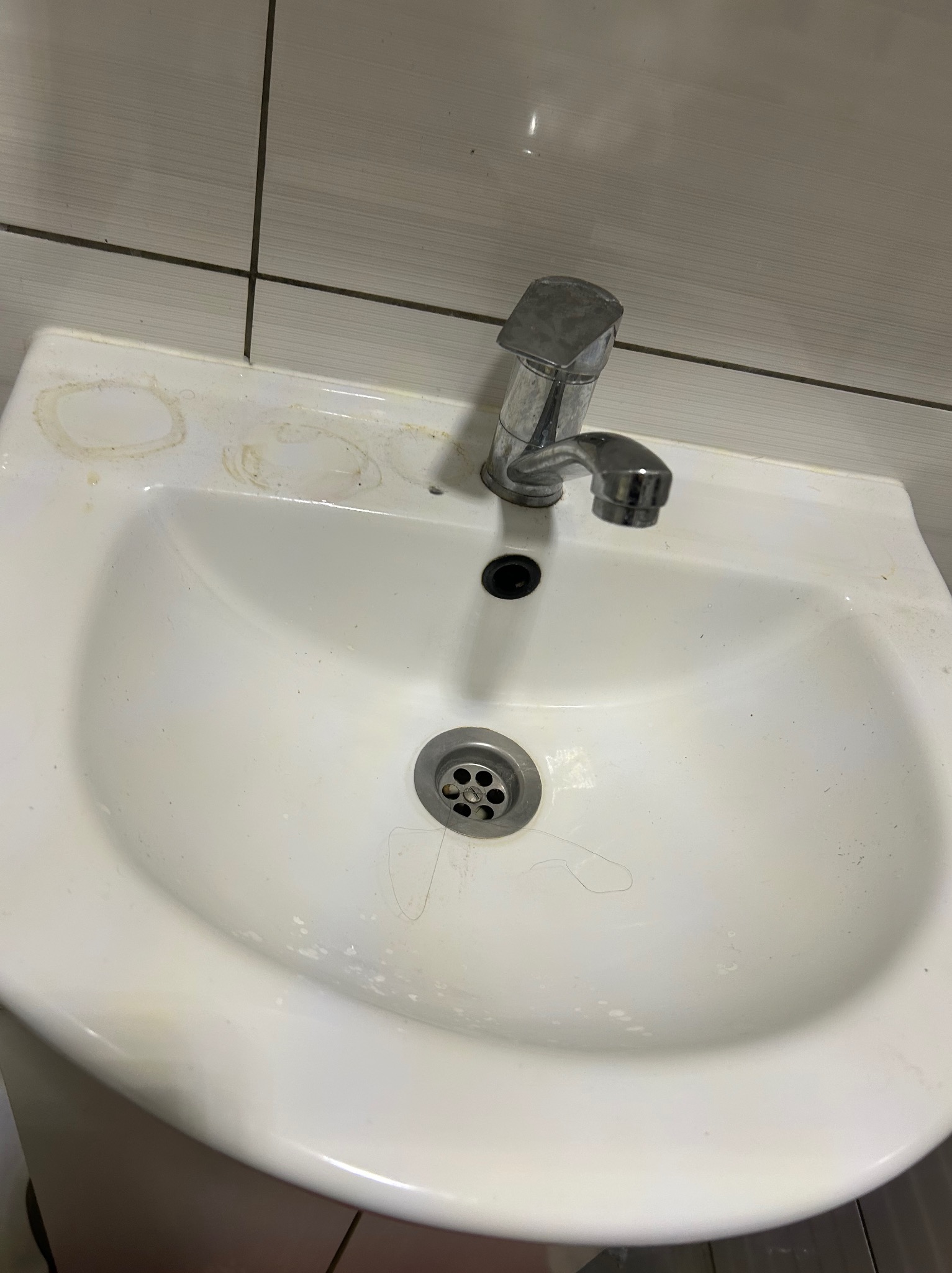 Zlew z widocznymi zabrudzeniami i osadami, ukazujący potrzebę dokładnego czyszczenia. Metalowa bateria z drobnymi śladami użytkowania. Ujęcie z góry.