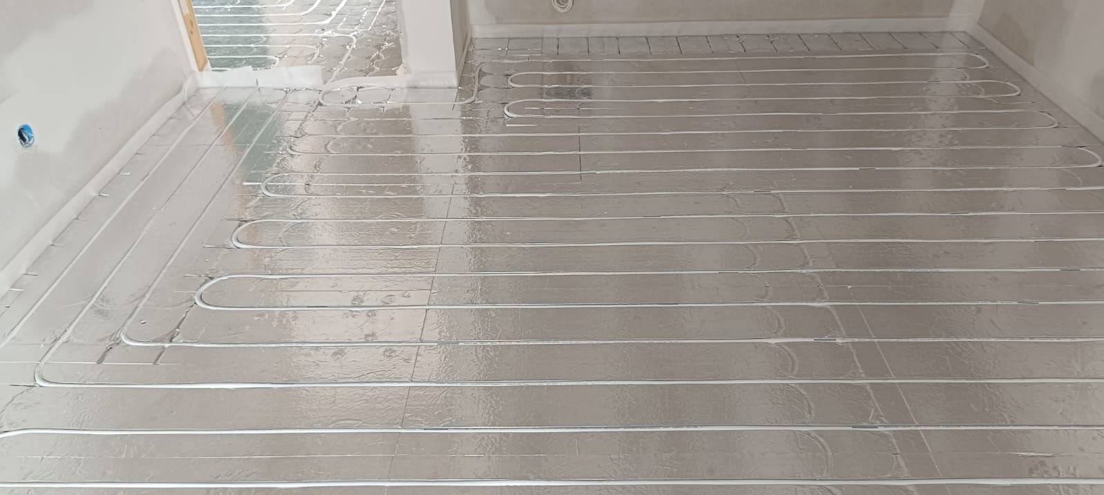 Ułożone rury ogrzewania podłogowego na srebrnej folii izolacyjnej w surowym wnętrzu. Widok z góry, równoległe ułożenie rur.