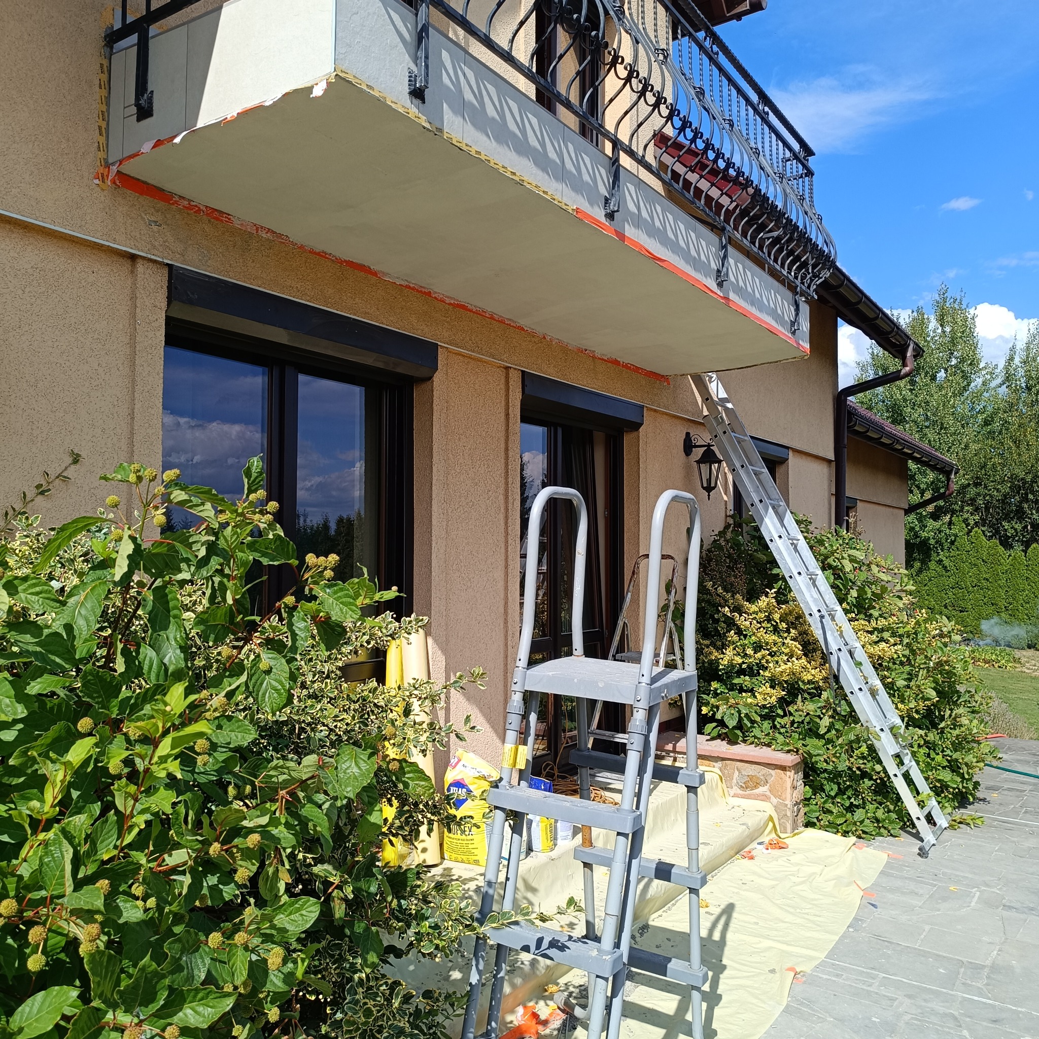 Prace remontowe balkonu w Bielanach: ocieplanie i przygotowanie do wykończenia. Widoczne rusztowania, materiały budowlane i zabezpieczenia.