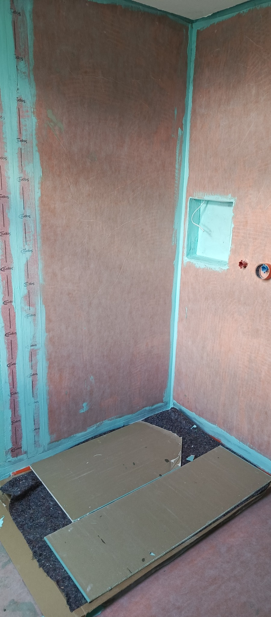 Przygotowanie ścian w łazience do położenia płytek: hydroizolacja z uszczelnieniem narożników i taśmą brzegową Sopro. Na podłodze płyty zabezpieczające.