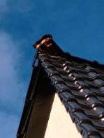 Fragment dachu z czarną dachówką ceramiczną, widoczny z dołu na tle błękitnego nieba. Ujęcie z niskiej perspektywy podkreśla strukturę i kolorystykę pokrycia.