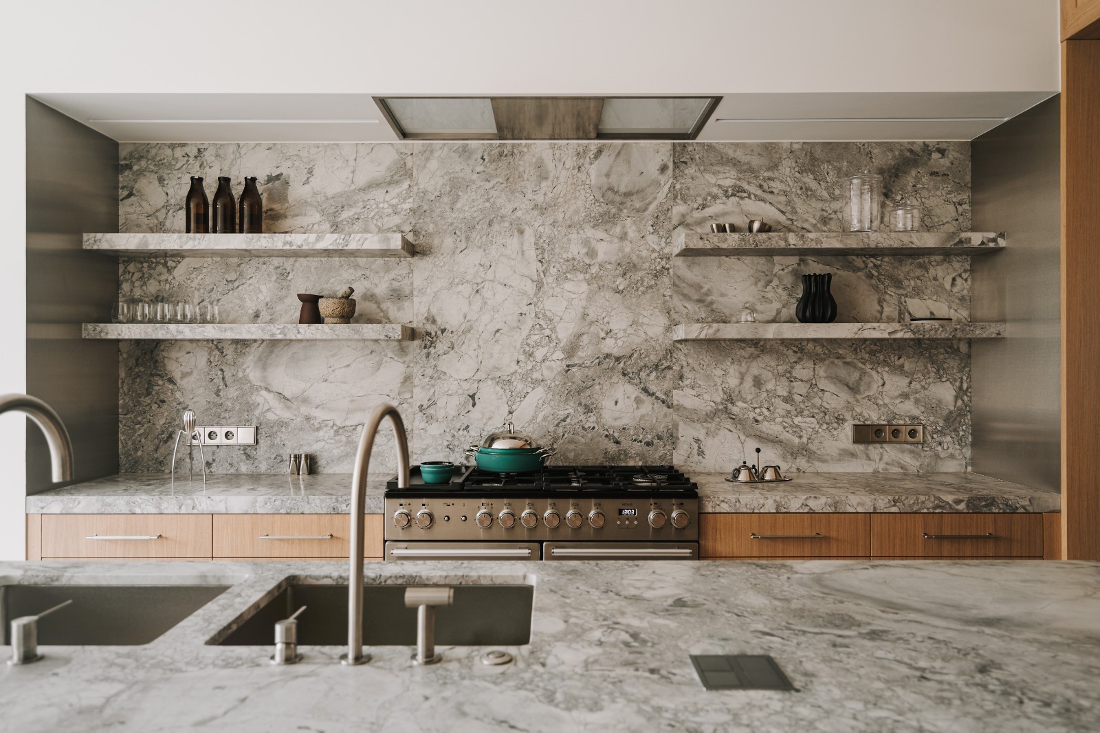 Kuchnia z blatem i ścianą z szarego marmuru. Na blacie kuchenka gazowa, na półkach naczynia i dekoracje. Minimalistyczny design z naturalnym kamieniem.