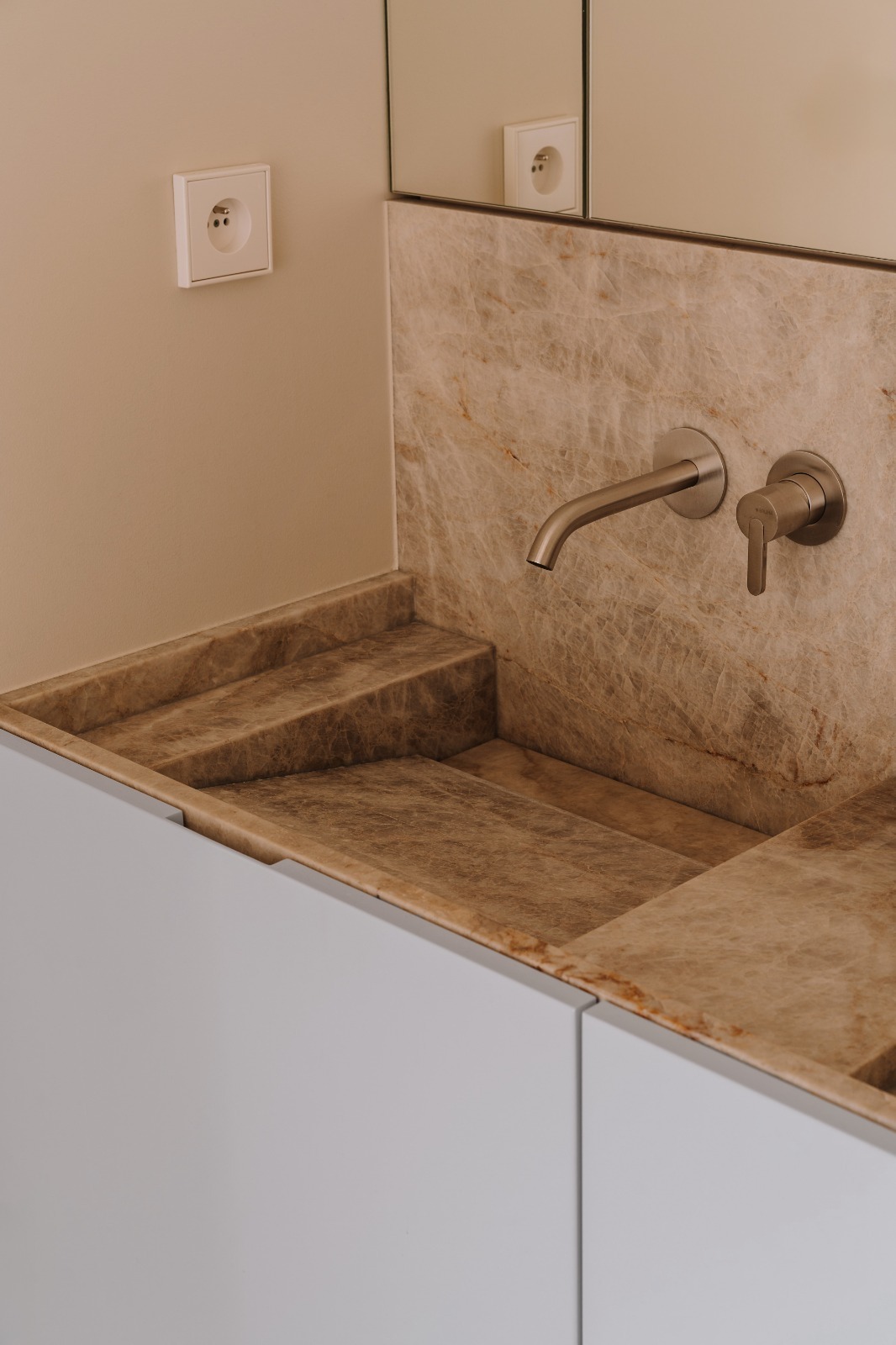 Marmurowa umywalka z baterią w minimalistycznej łazience. Widoczny fragment szafki pod umywalką, gniazdko i lustro. Ujęcie z góry, podkreślające unikalny wzór kamienia.