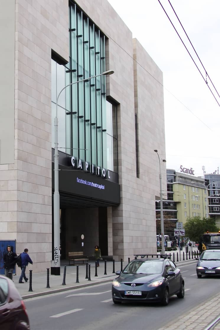 Elewacja budynku Capitol we Wrocławiu, wykończona jasnym kamieniem z dużymi oknami. Widoczny fragment ulicy z samochodami i przechodniami.