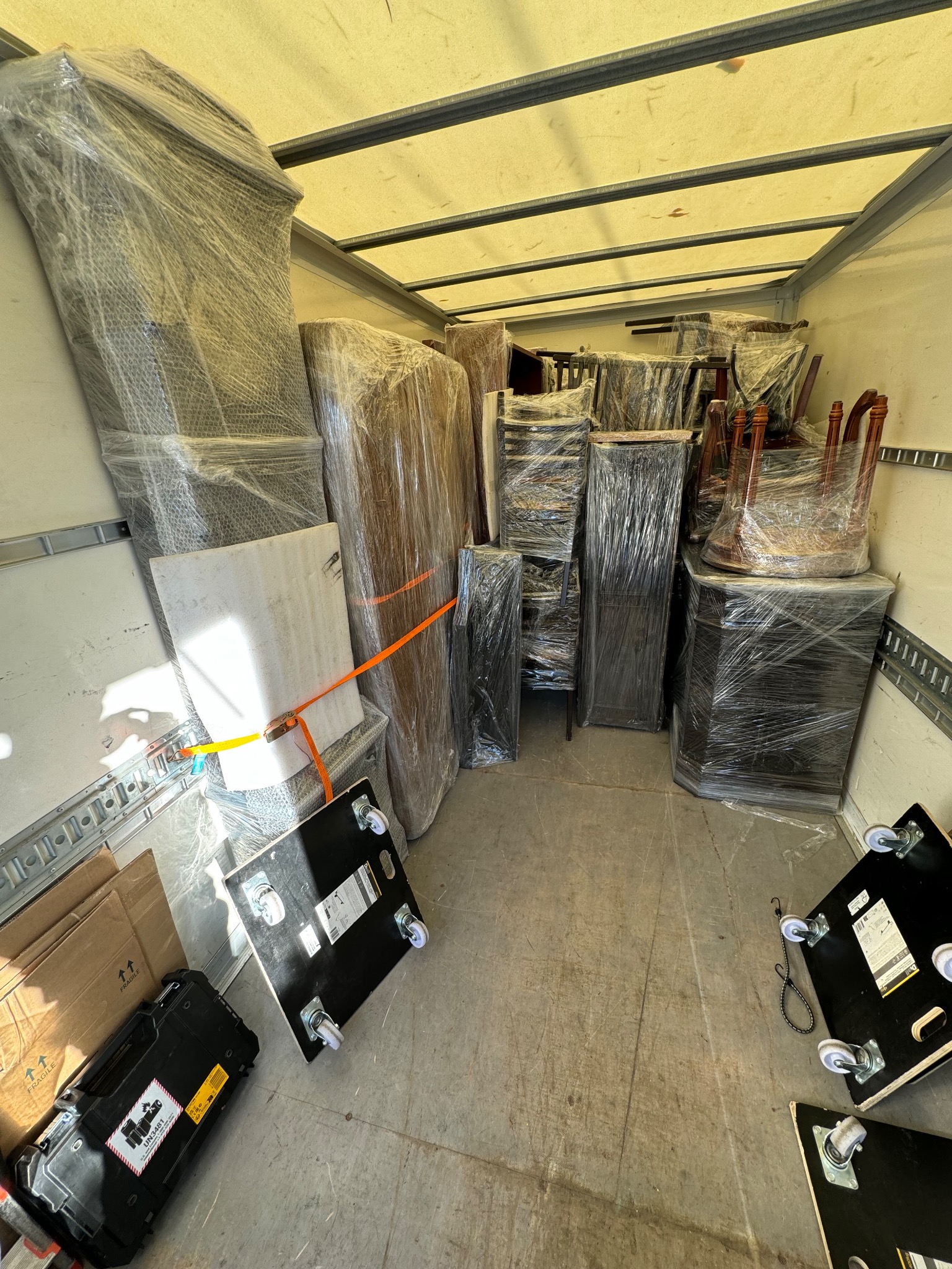 Meble zabezpieczone folią stretch wewnątrz przestrzeni ładunkowej pojazdu transportowego, gotowe do przewozu. Widoczne pasy mocujące i wózki transportowe.