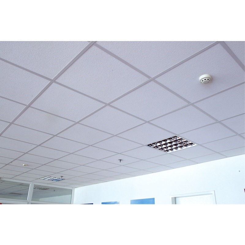 Biały sufit podwieszany z rastrowym oświetleniem i czujnikiem dymu, widok z dołu. Regularna siatka profili tworzy kwadratowe pola.