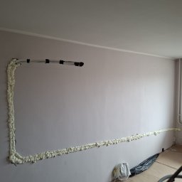 BG KLIMATYZACJA Bogdan Głowacz - Montaż instalacji klimatyzacyjnej: rury przymocowane do ściany, zabezpieczone pianką montażową. Widoczne narzędzia i przygotowane podłoże.