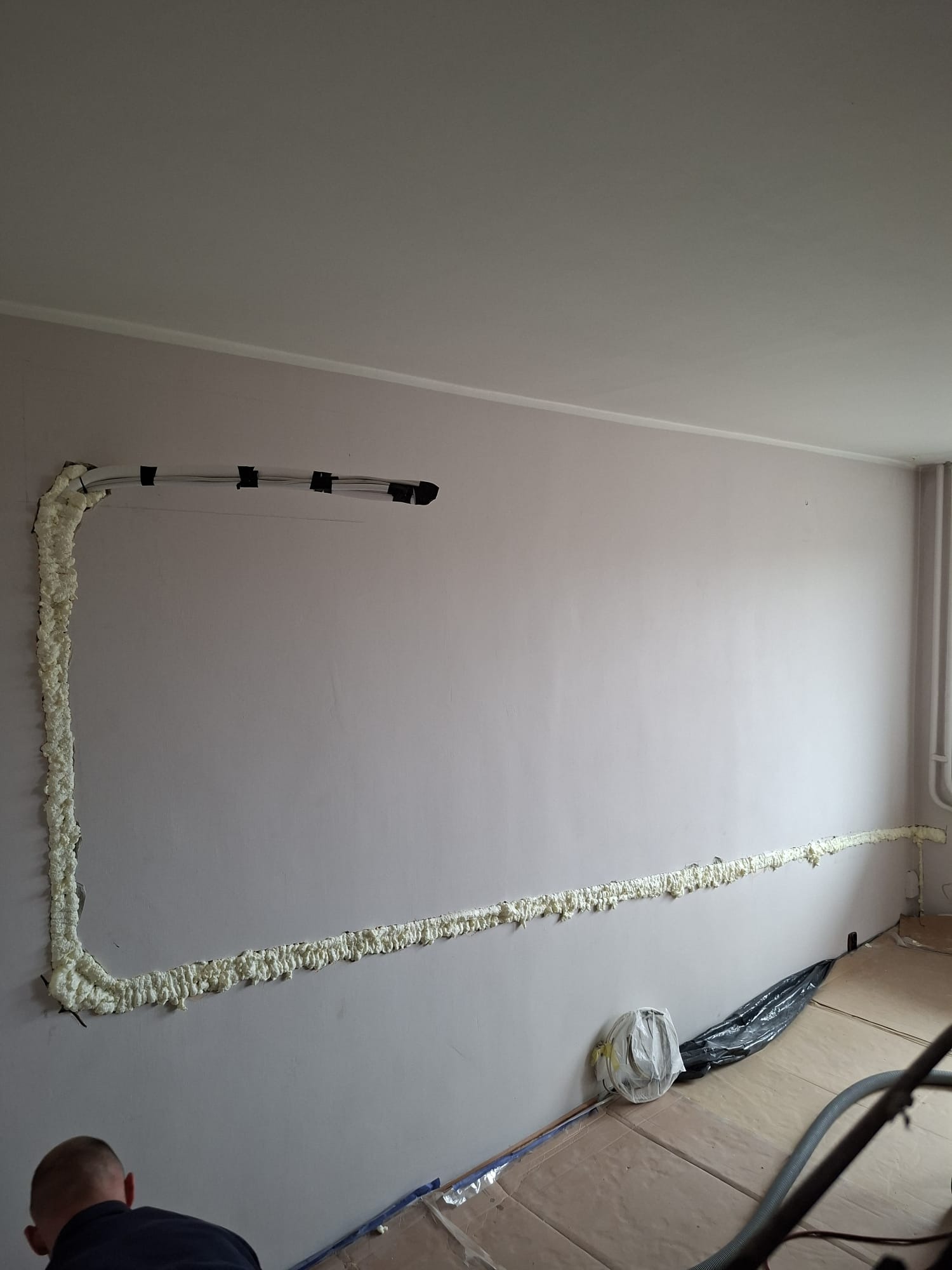 Montaż instalacji klimatyzacyjnej: rury przymocowane do ściany, zabezpieczone pianką montażową. Widoczne narzędzia i przygotowane podłoże.