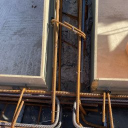 Usługi Budowlane, Klimatyzacje Mariusz Soboniak - Zbrojenie fundamentów w szalunku, widok z góry. Stalowe pręty połączone drutem, beton w tle. Etap budowy domu, przygotowanie do zalewania betonem.