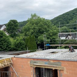 Usługi Budowlane, Klimatyzacje Mariusz Soboniak - Budowa domu z czerwonej cegły: pracownik montuje zbrojenie na stropie. Widoczne szalunki, rusztowania i zielone wzgórza w tle. Ujęcie z góry, w dzień.