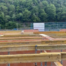 Usługi Budowlane, Klimatyzacje Mariusz Soboniak - Budowa domu: widok na fundamenty z czerwonej cegły i drewniane szalunki Doka H20 3.30m. W tle zieleń drzew i rusztowania.