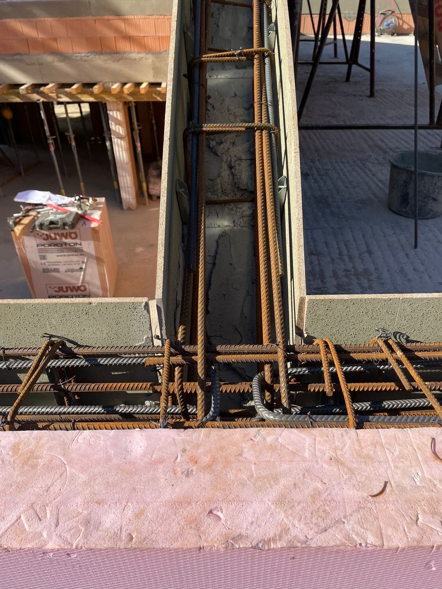 Zbrojenie pionowe i poziome w szalunku, widoczne pręty stalowe i beton. W tle bloczki Ytong i elementy konstrukcji. Detal budowy domu z betonu komórkowego.