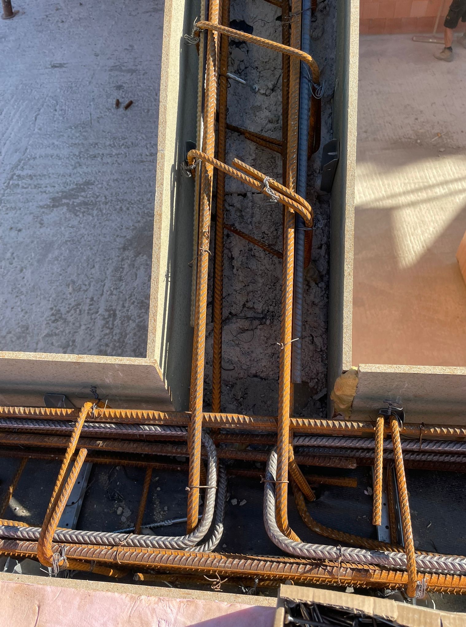 Zbrojenie fundamentów w szalunku, widok z góry. Stalowe pręty połączone drutem, beton w tle. Etap budowy domu, przygotowanie do zalewania betonem.