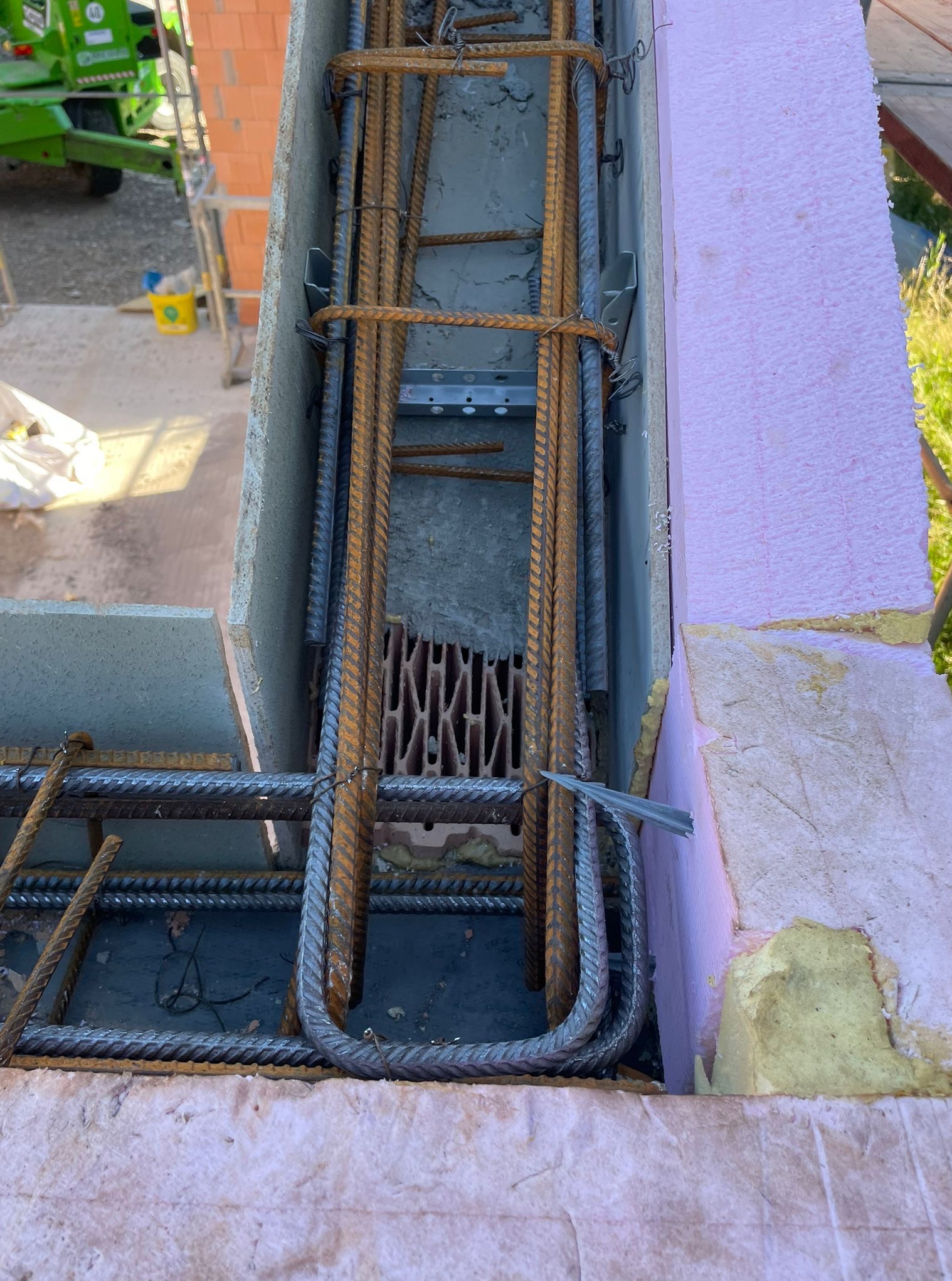 Zbrojenie w szalunku z izolacją styropianową, widok z góry. Stalowe pręty zbrojeniowe, szare ściany szalunku i różowy styropian tworzą kontrastującą kompozycję.