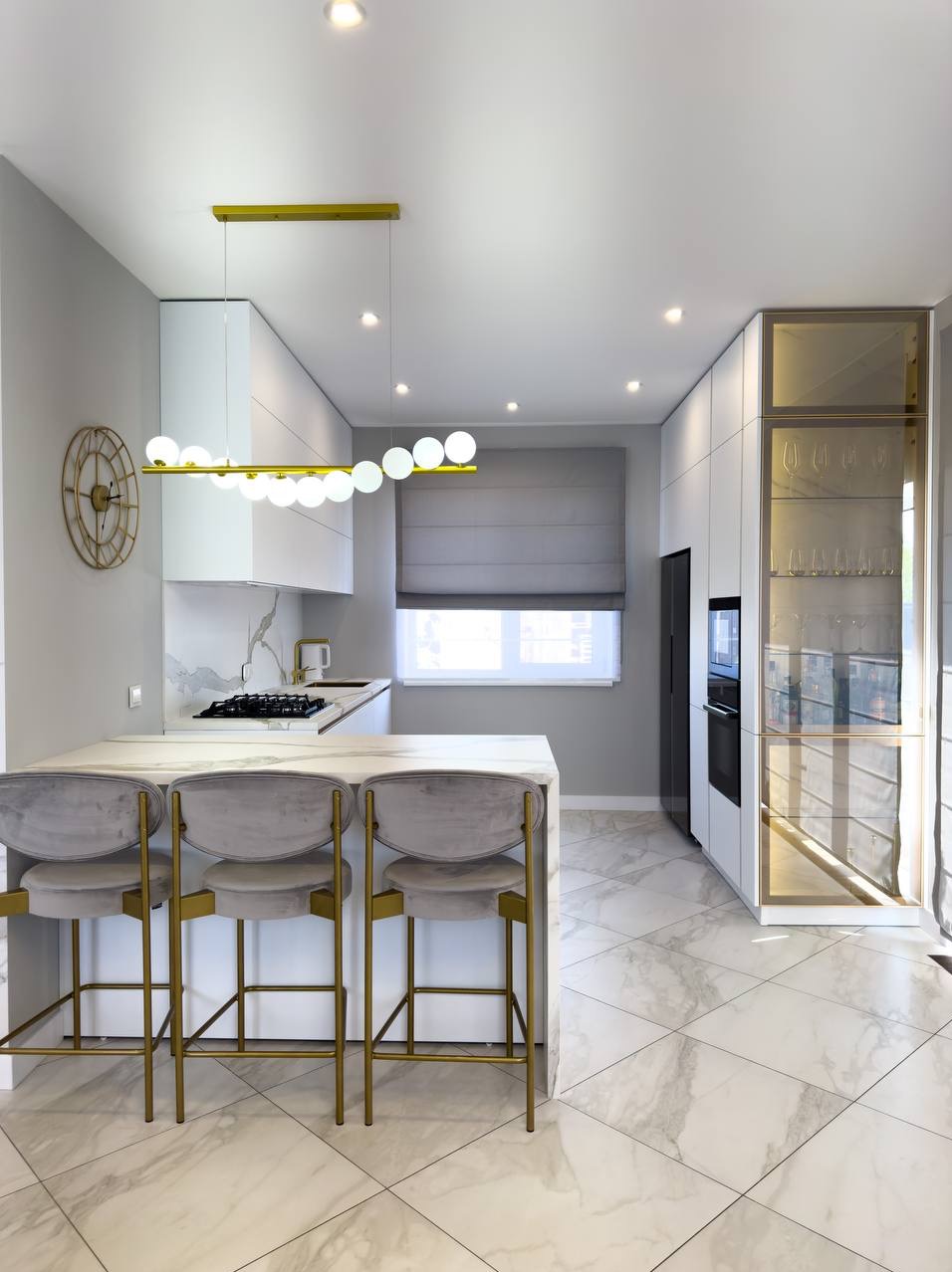 Nowoczesna kuchnia z wyspą i marmurową podłogą. Złoty zegar na ścianie, designerska lampa nad wyspą. Minimalistyczne szafki i szklana witryna.