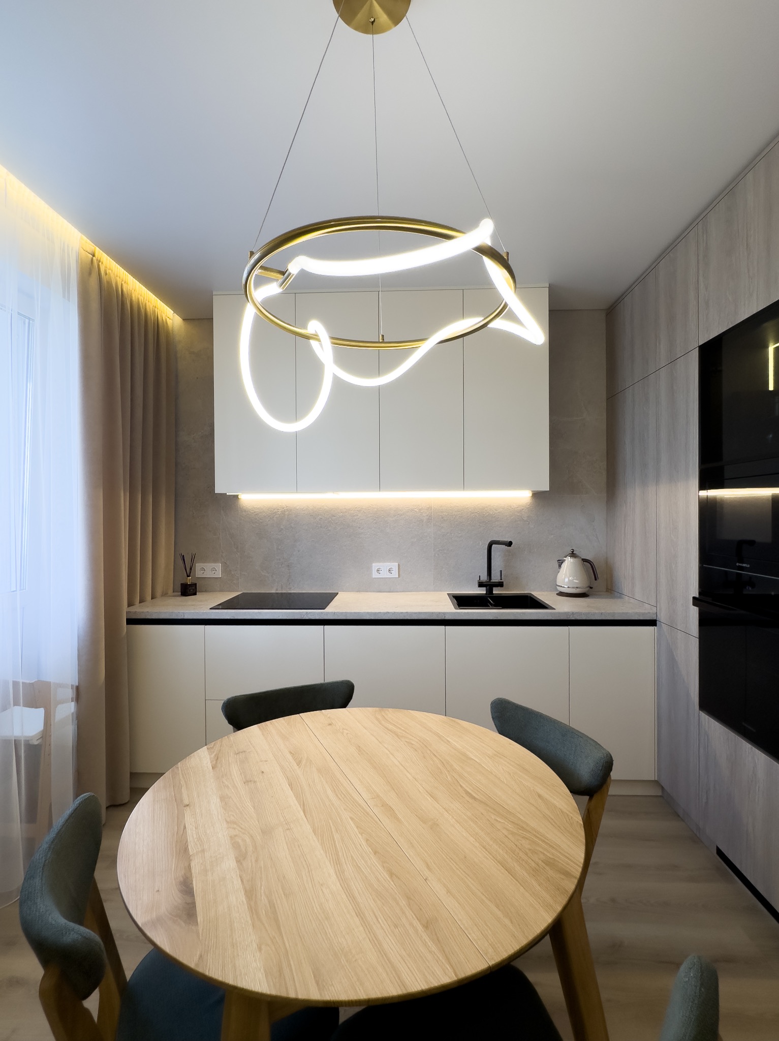 Nowoczesna kuchnia z okrągłym stołem i designerską lampą sufitową. Białe szafki, szare panele ścienne i podświetlenie LED tworzą elegancki wystrój wnętrza.