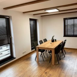 Palk-Art Design - Jadalnia z trzema oknami z ciemnymi żaluzjami drewnianymi. Widok na zewnątrz z jednego okna. Drewniany stół i krzesła. Drewniane belki na suficie.