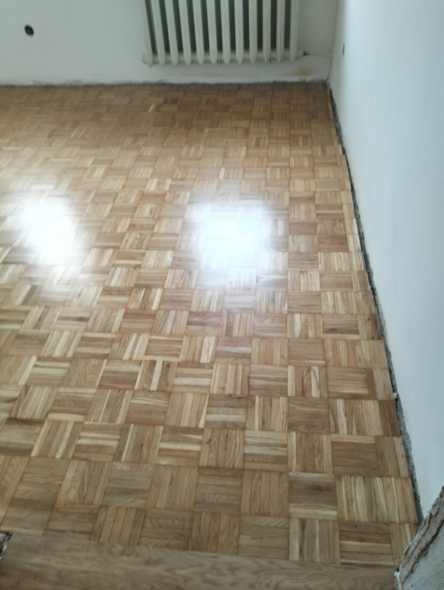 Ułożony parkiet w jodełkę francuską, widok z góry, jasne drewno, grzejnik na ścianie, świeżo położona podłoga, wykończenie podłogi.