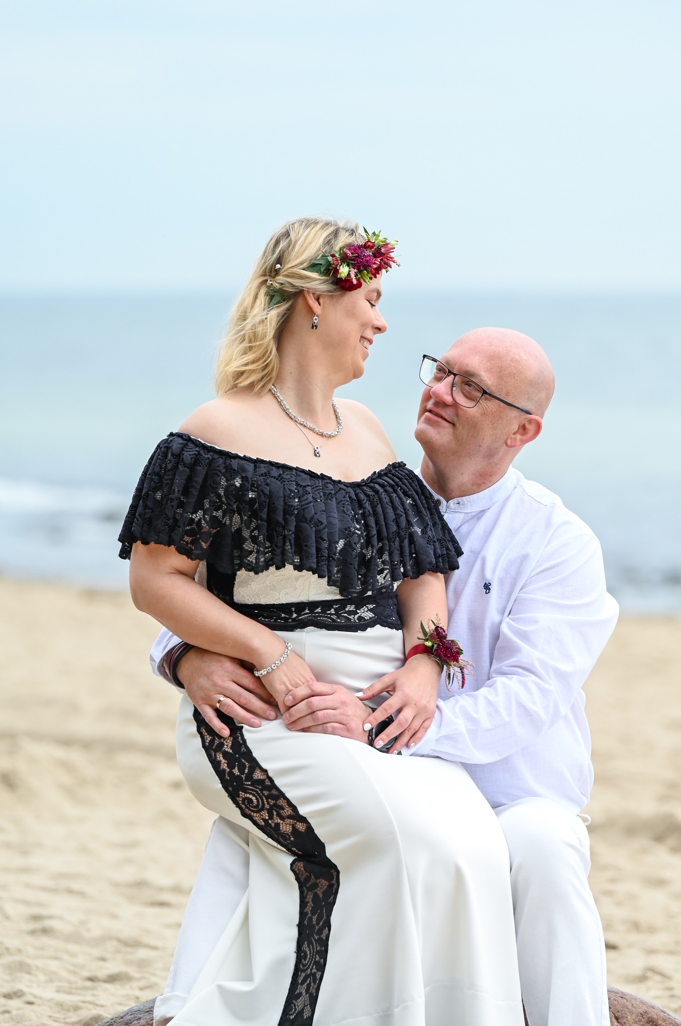 Para młoda na plaży: Panna młoda w sukni z koronką i wiankiem, pan młody w białej koszuli. Romantyczny portret zakochanych z morzem w tle, wykonany w naturalnym oświetleniu.