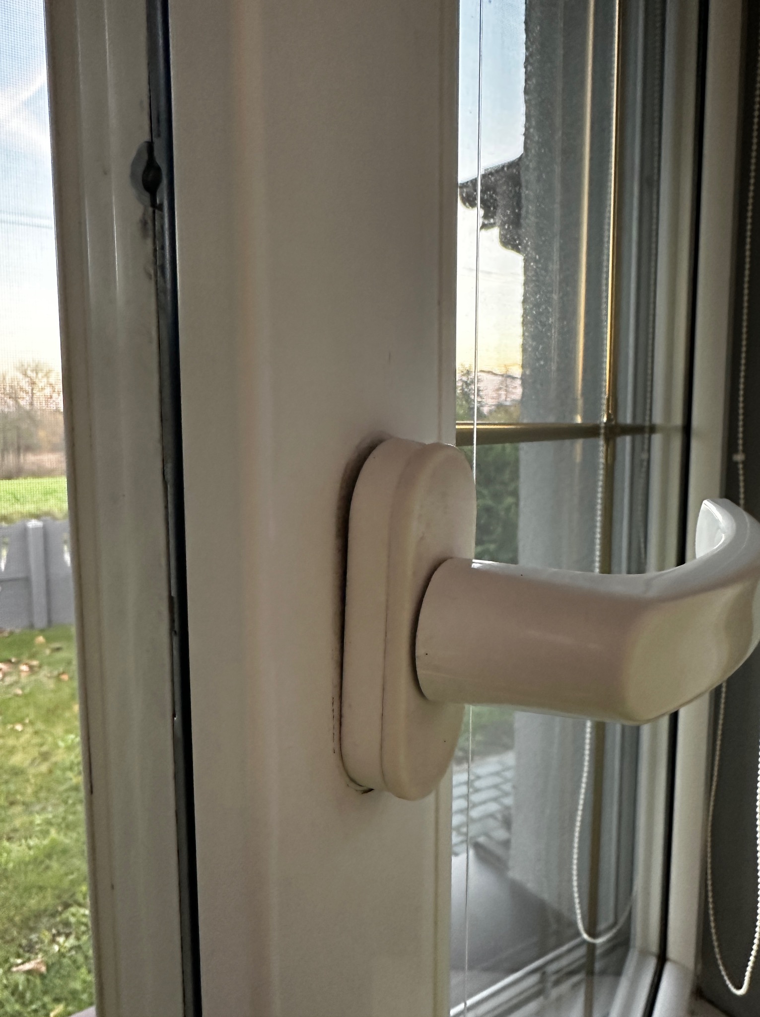Otwarty fragment okna PCV z widocznym uchwytem i fragmentem krajobrazu za oknem. Widoczne zabrudzenia na ramie okiennej.