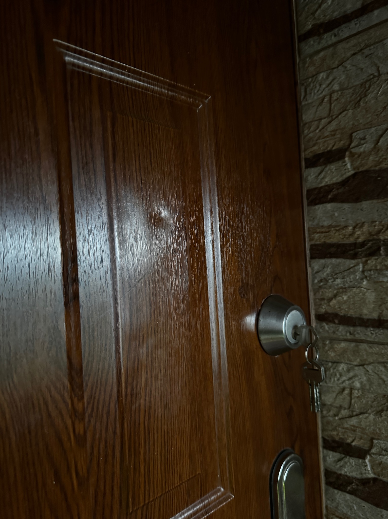 Lakierowane, drewniane drzwi wejściowe z zamkiem i kluczem, widoczne z bliska, z fragmentem kamiennej ściany w tle. Detal wykończenia wnętrza.
