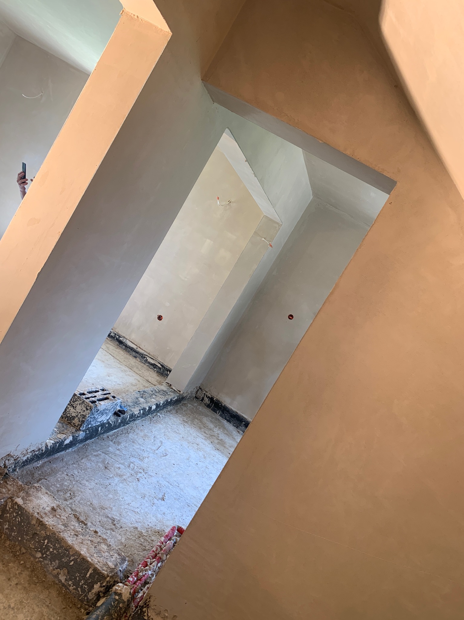 Wnętrze w trakcie prac wykończeniowych: świeżo nałożone, gładkie tynki na ścianach i suficie, widoczne elementy instalacji elektrycznej. Ujęcie z dołu, perspektywa.