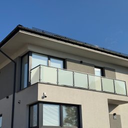 MastMet - Nowoczesny balkon z szklaną balustradą w budynku o minimalistycznej architekturze, oświetlony jasnym, naturalnym światłem słonecznym. Widoczny numer domu 127.