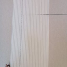 KASKADA PŁYTEK Kamil Stępień - Ściana z zamontowaną listwą dekoracyjną z pionowymi żłobieniami i taśmą LED. Widoczny fragment instalacji elektrycznej.