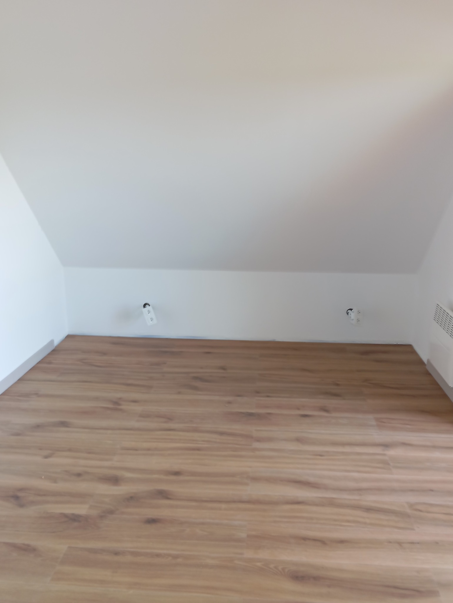 Jasne panele podłogowe w pokoju na poddaszu z białymi ścianami i widocznymi gniazdkami. Ukończona podłoga w nowym wnętrzu.