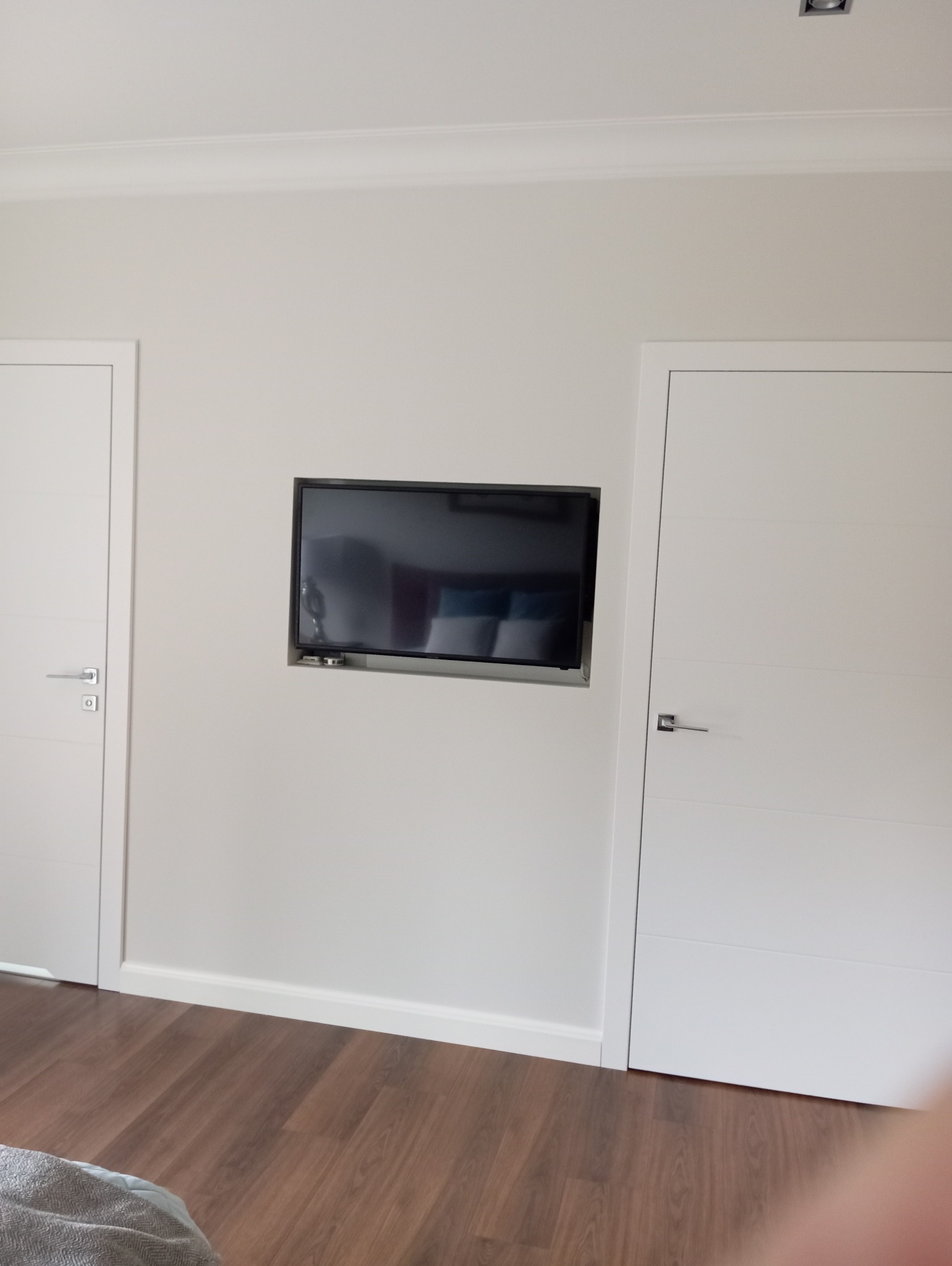 Minimalistyczne wnętrze: Telewizor w ścianie między białymi drzwiami, brązowe panele podłogowe, listwy przypodłogowe. Nowoczesny design.