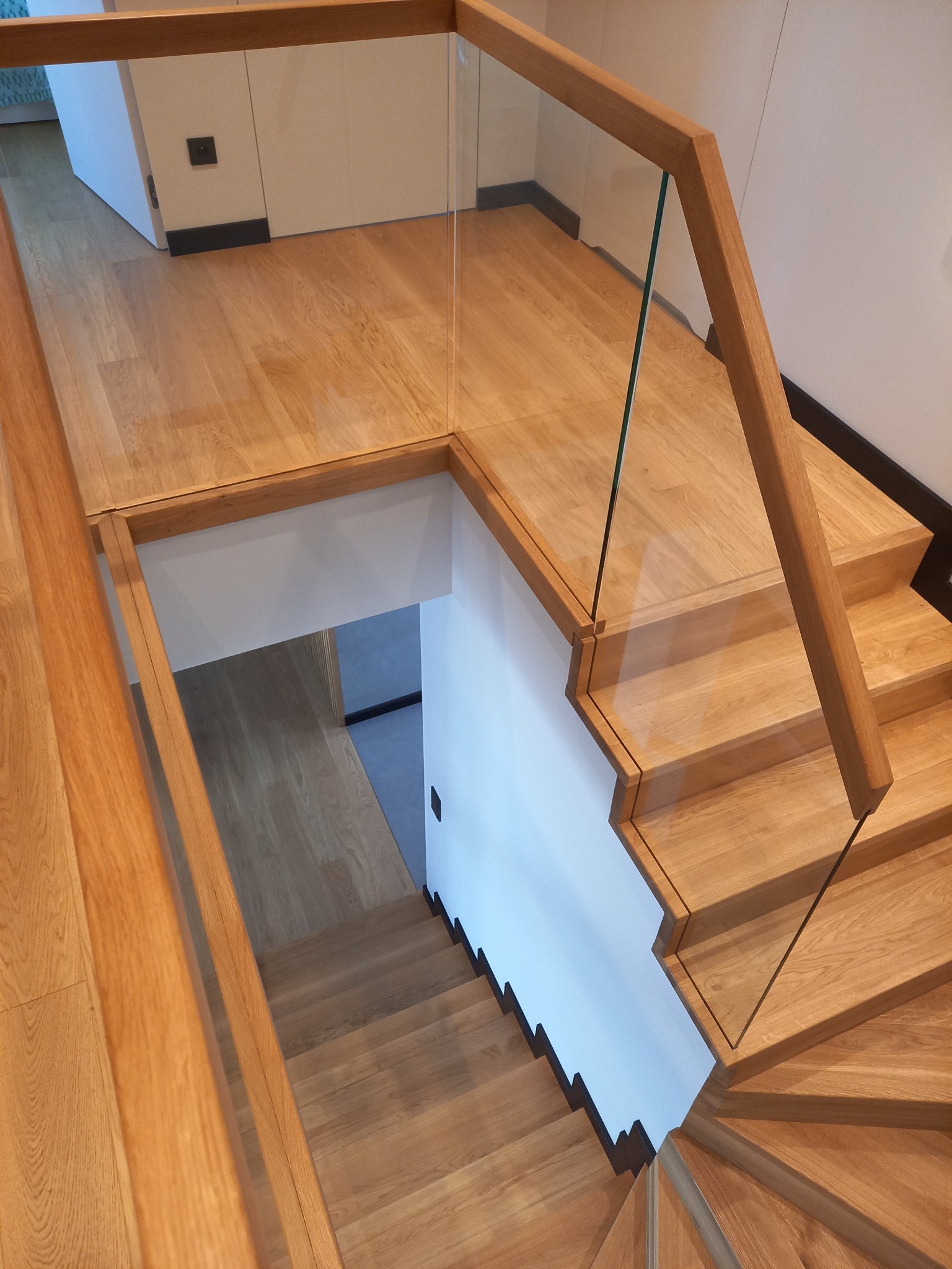 Drewniane schody z jasnego drewna z nowoczesną balustradą ze szkła, widok z góry, naturalne oświetlenie, minimalistyczny design.