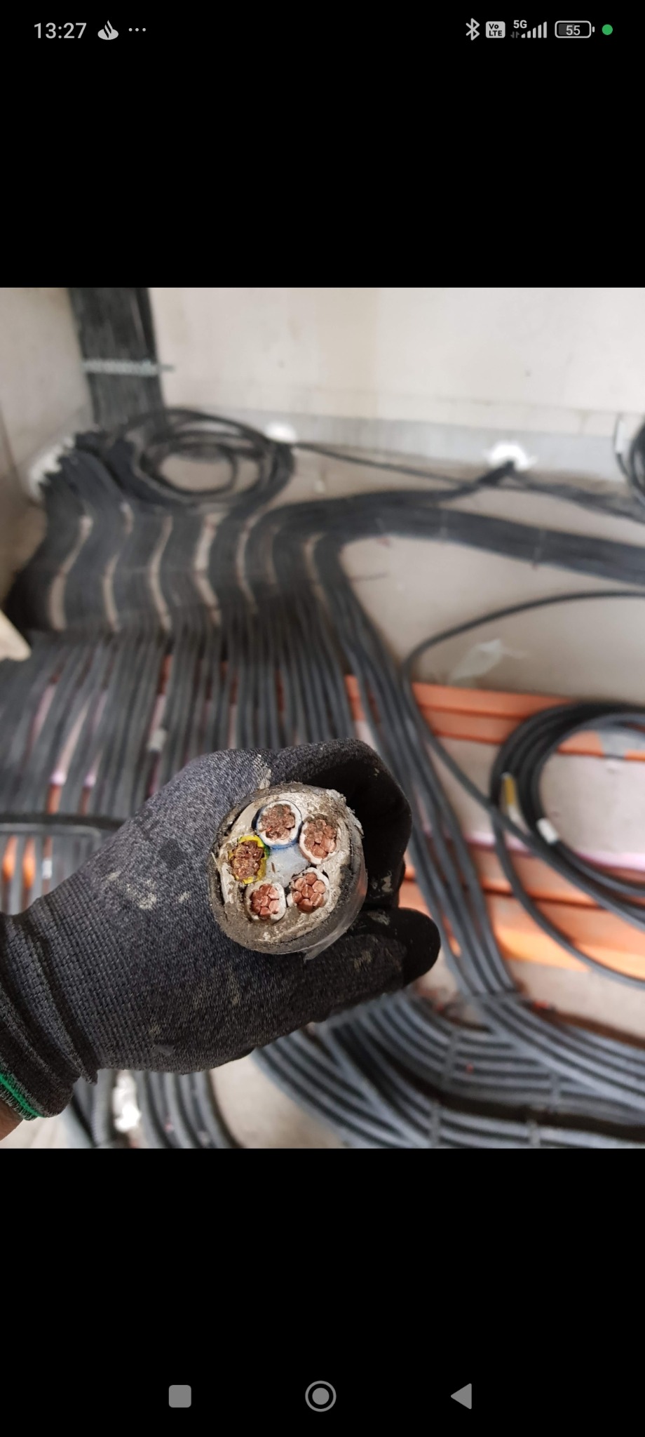 Przekrój grubego kabla elektrycznego z miedzianymi żyłami, trzymanego w rękawicy roboczej. W tle wiązki kabli ułożone wzdłuż ściany.