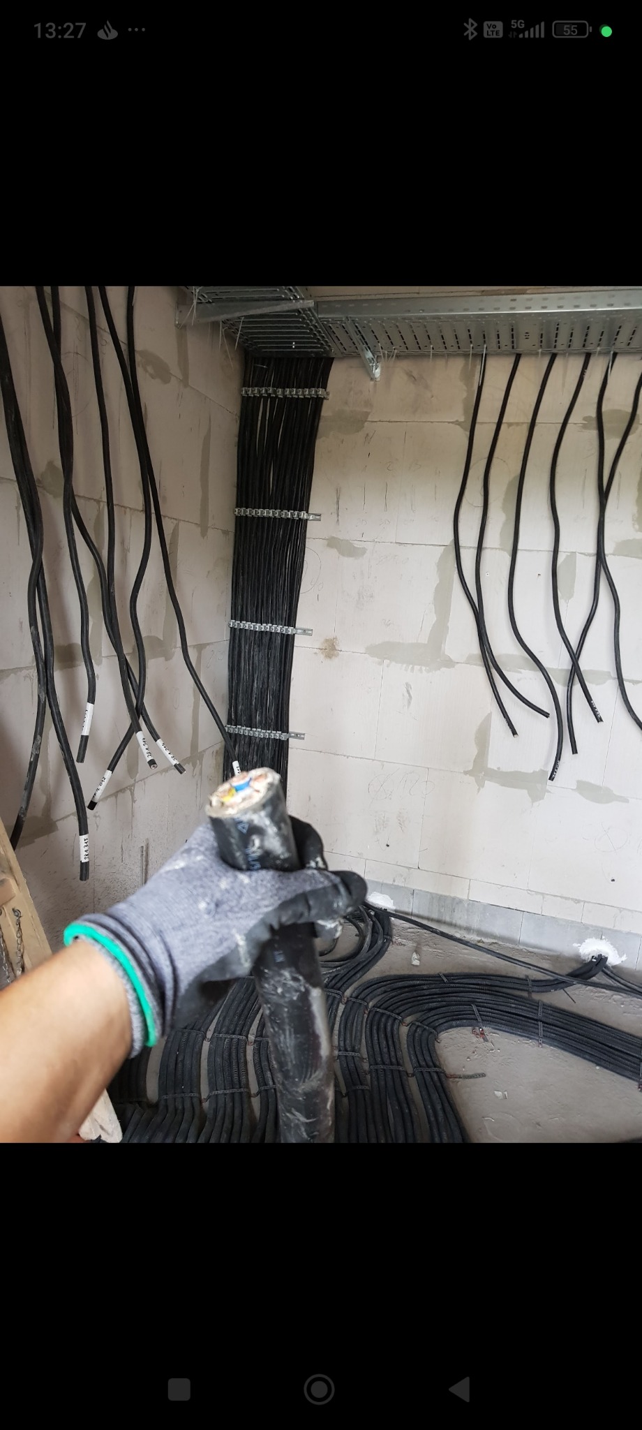 Rozprowadzone kable elektryczne w korytach i na ścianie z betonu komórkowego. W dłoni w rękawicy kabel z widocznym przekrojem żył.