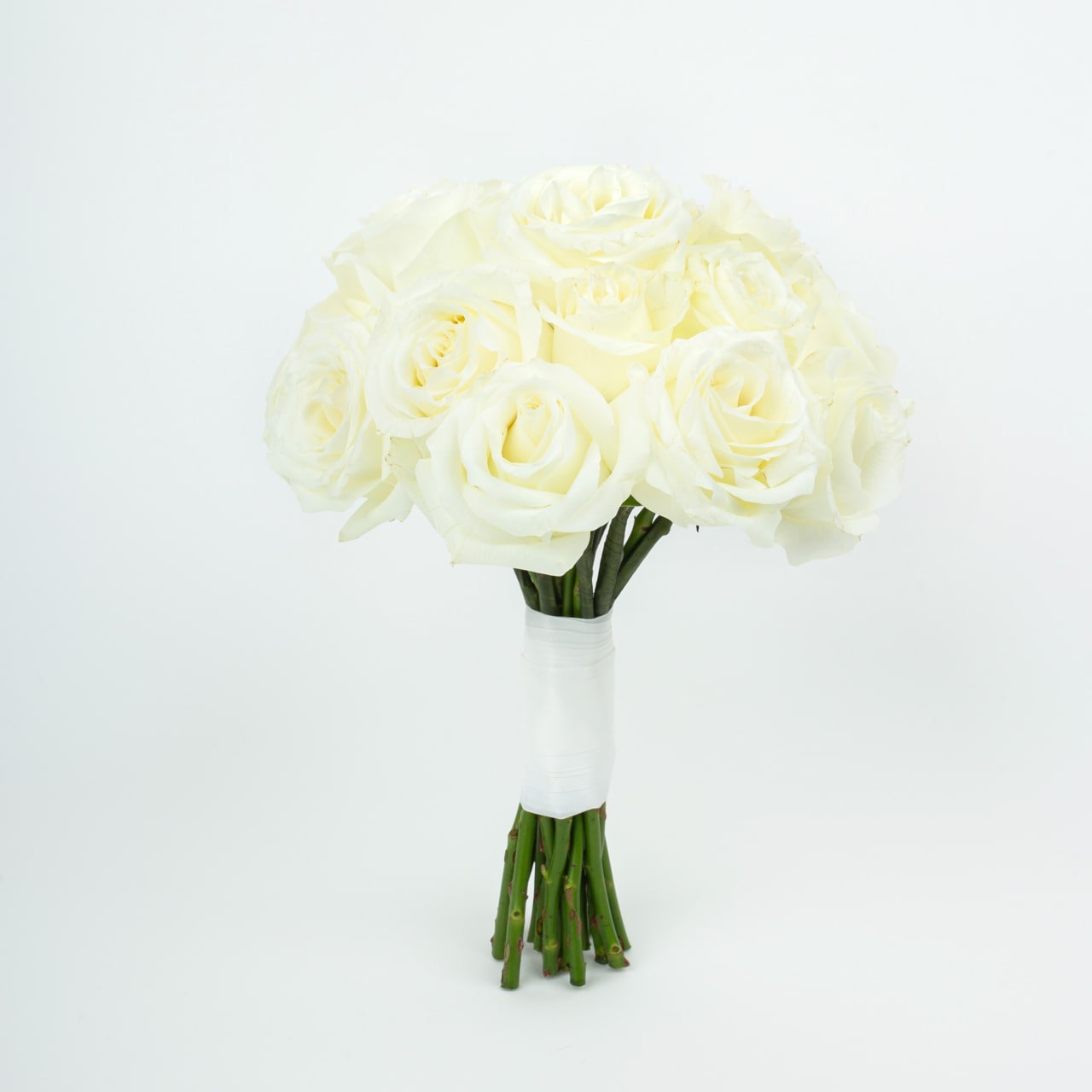 Bukiet ślubny z białych róż, związany białą wstążką. Minimalistyczne tło podkreśla delikatność kwiatów. Widoczne zielone łodygi i subtelne detale płatków.