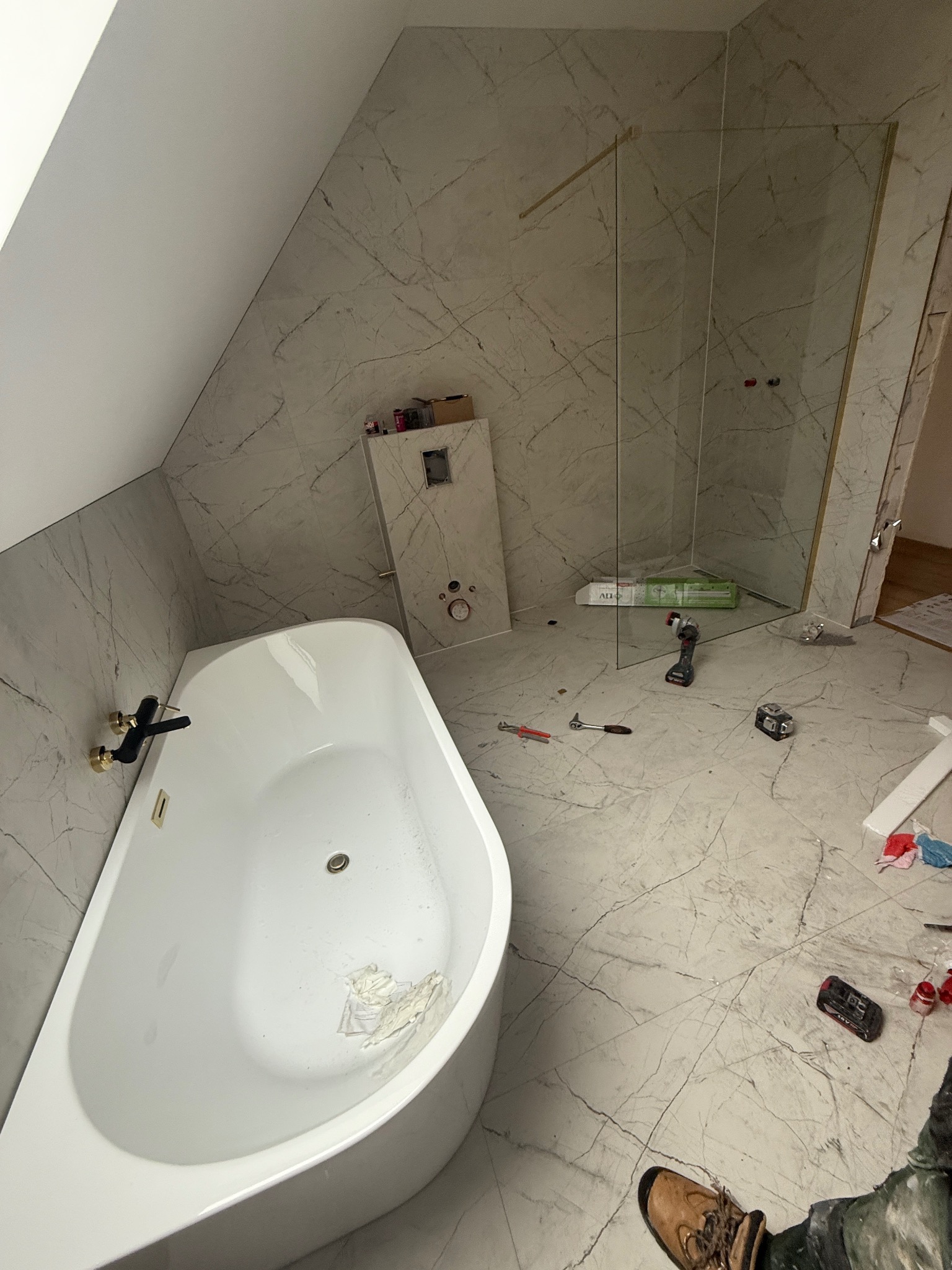 Montaż kabiny prysznicowej w łazience z marmurowymi płytkami w Gdańsku. Widoczna wanna z czarną armaturą i narzędzia pracy.