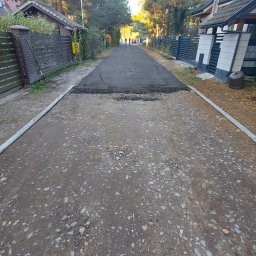 P.H.T.U - Fragment utwardzonej drogi dojazdowej na osiedlu domów jednorodzinnych. Widoczne świeże asfaltowanie na tle istniejącej nawierzchni. Prace w toku.