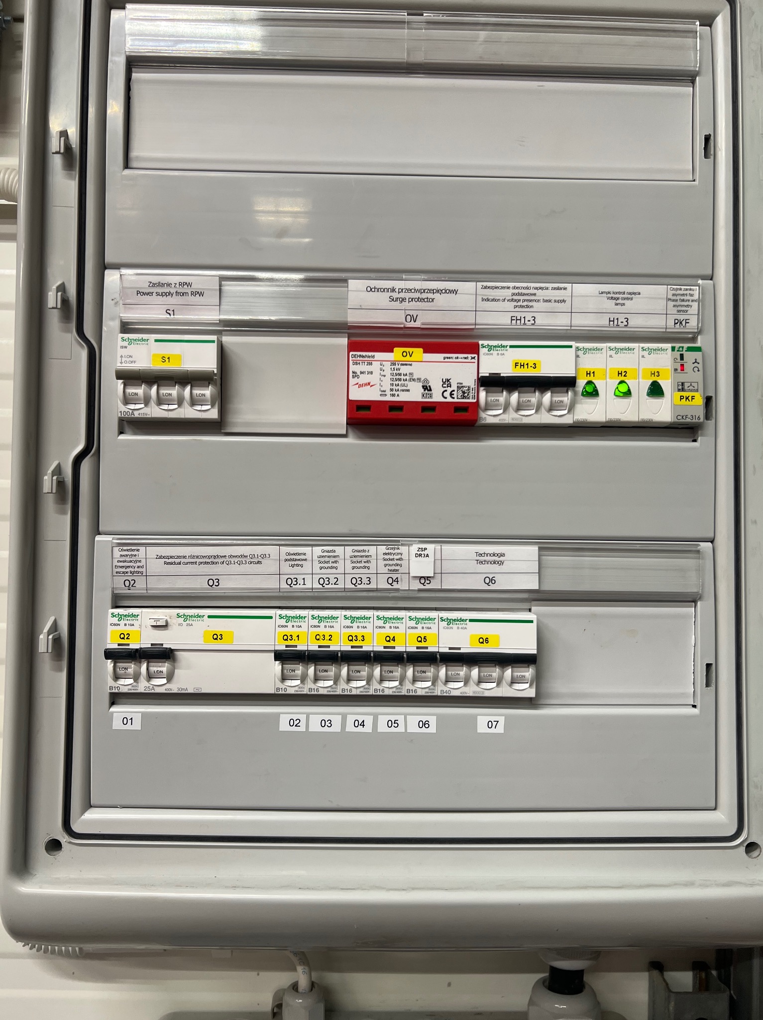 Szczegółowe ujęcie rozdzielnicy elektrycznej Schneider z zabezpieczeniami, wyłącznikami i oznaczeniami. Widoczne elementy instalacji elektrycznej w szarej obudowie.