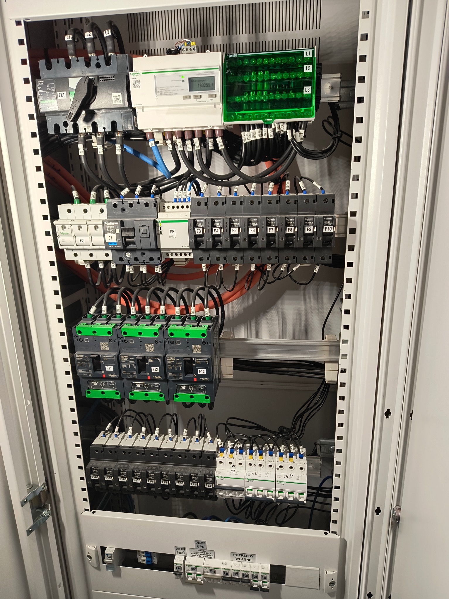 Rozdzielnica elektryczna w metalowej obudowie, widoczne zabezpieczenia, liczniki i okablowanie. Elementy Schneider Electric. Instalacja po montażu, gotowa do użytku.