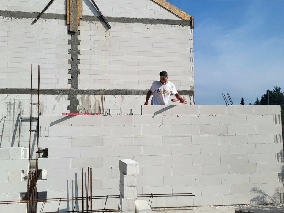 Budowa domu z białych bloczków w Lubinie. Murarz z poziomicą kontroluje ułożenie warstwy. Widoczne zbrojenia i elementy konstrukcyjne.