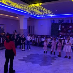 Mimifun - Dzieci aktywnie bawiące się na parkiecie oświetlonym niebiesko-żółtym światłem, pod sufitem z efektem gwiazd. W tle stół z dekoracją '1' i goście.