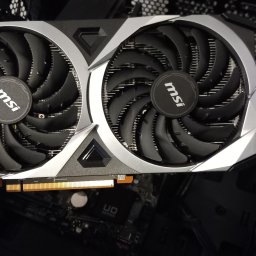 HUBICHEM Hubert Wodnicki - Karta graficzna MSI z dwoma wentylatorami, częściowo zamontowana w obudowie komputera. Widoczny fragment płyty głównej. Ujęcie z bliska, z ręką trzymającą kartę.