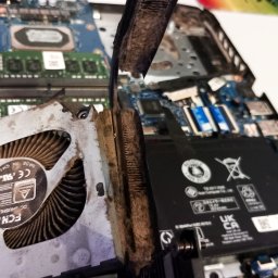 HUBICHEM Hubert Wodnicki - Otwarty laptop z widocznym, zakurzonym układem chłodzenia (wentylator i radiator) podczas czyszczenia. Widoczne elementy płyty głównej i baterii.