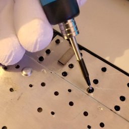 HUBICHEM Hubert Wodnicki - Wkręcanie śrubki w obudowę klawiatury laptopa za pomocą precyzyjnego wkrętaka, dłoń w białej rękawiczce. Detal naprawy elektroniki, bliskie ujęcie.